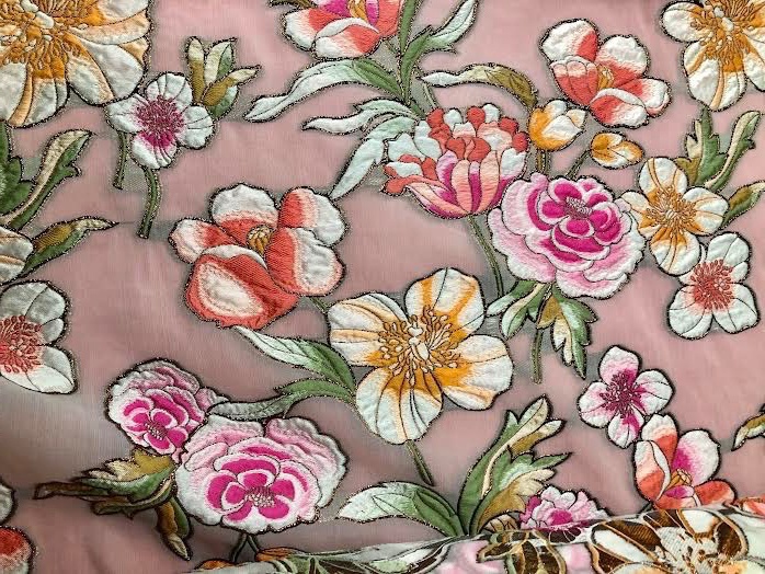 Pink, yellow, and orange flowers appear to be embroidered onto a pink fabric.