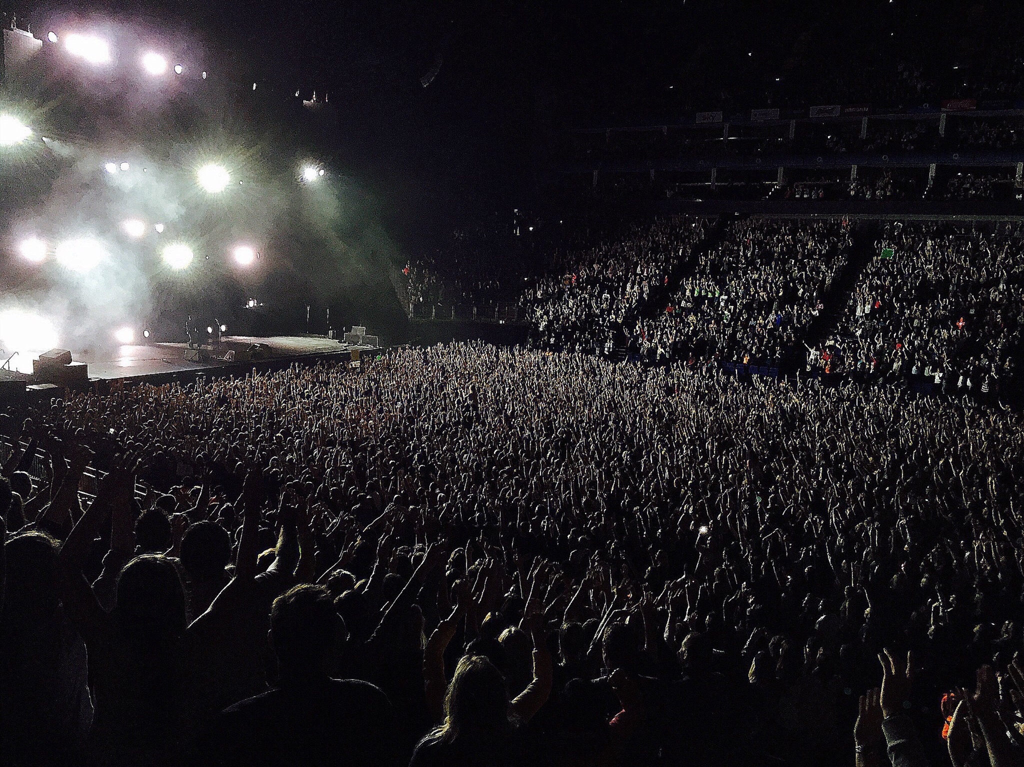 A crowd at an arena concert with a stage in front of the audience