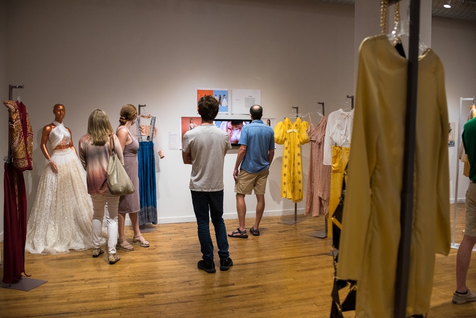 Several people look through a gallery filled with mannequins displaying garments.