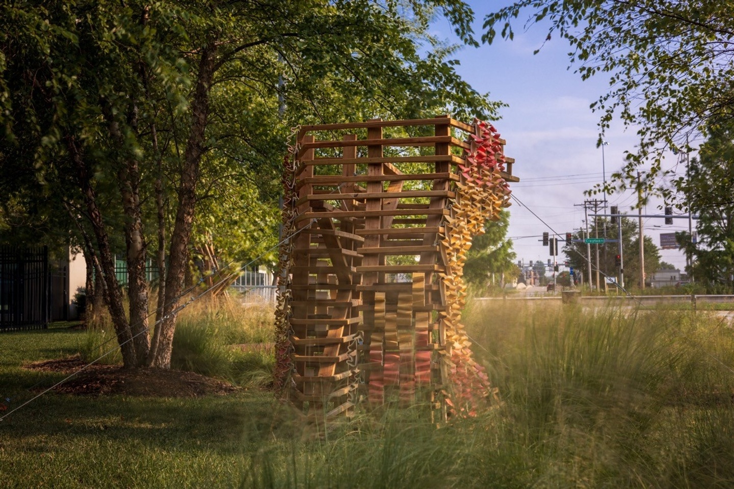 Wood and ceramic sculpture outdoors next to tree and native grasses