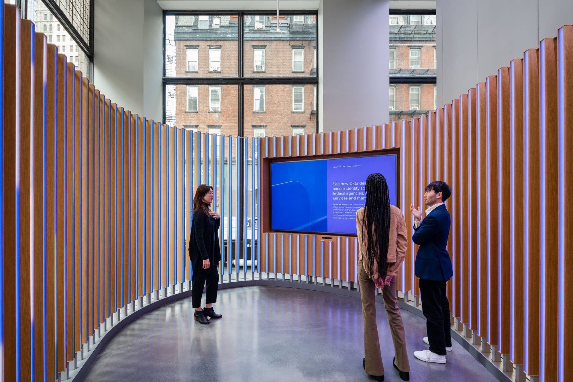 Three visitors at the sales center on the interior of the installation, looking at content on a large digital screen