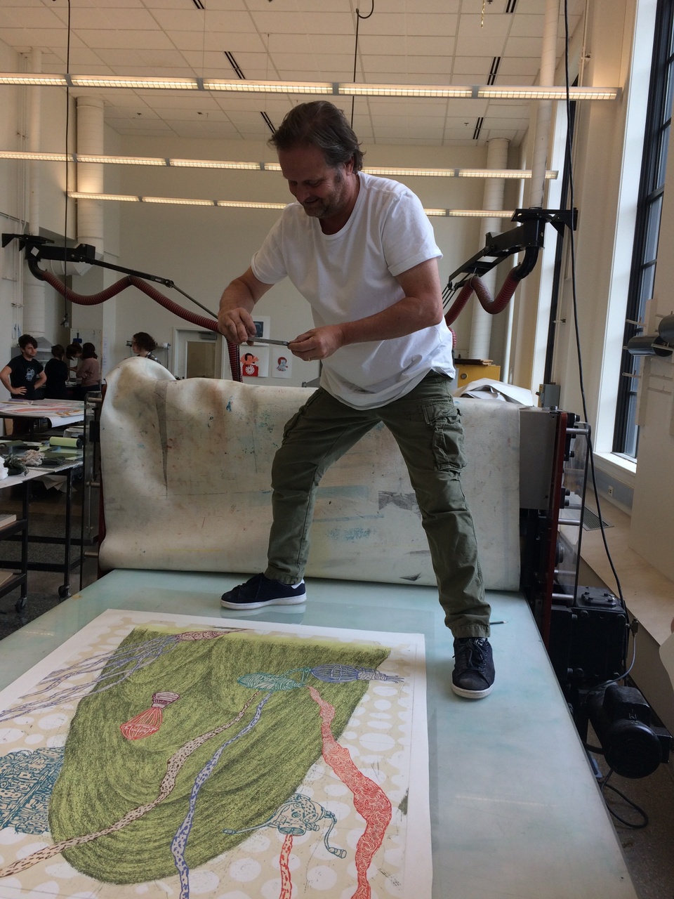 artist standing on top of the printing press to take a picture of a proof of his print