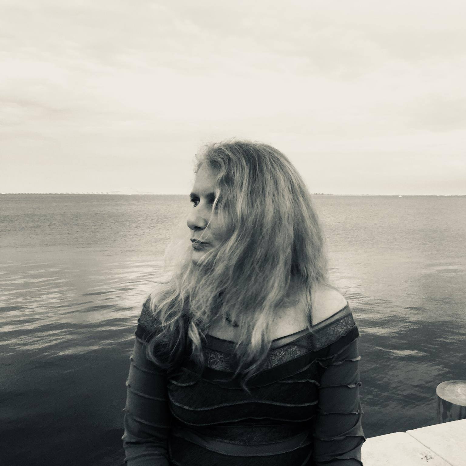 A woman with long dirty blond hair sitting on the edge of a large body of water