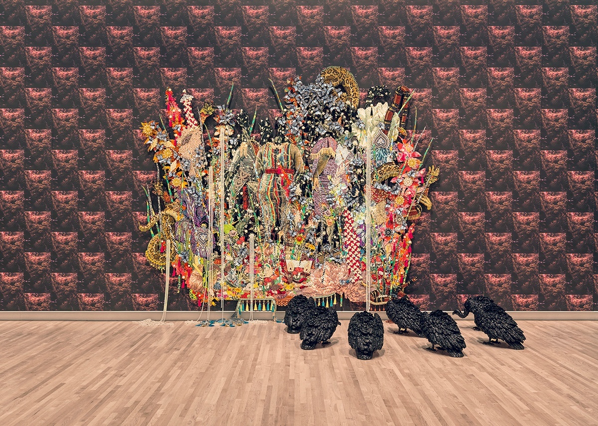 Ornate, bejeweled artwork on patterned wallpaper with black bird figures on the floor in front