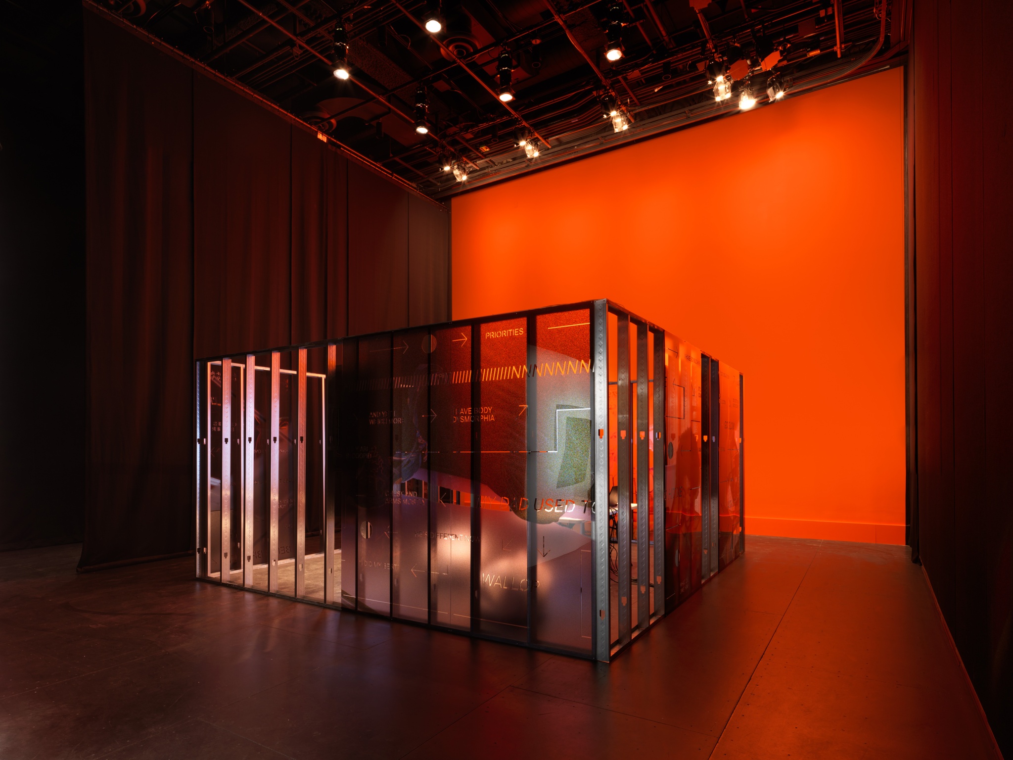 A view of an art installation by Martine Syms of the steel framework of a room's walls against a bright orange background