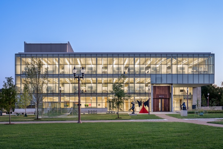 Three story glass walled building with a cantilever on one corner and large wooden doors.