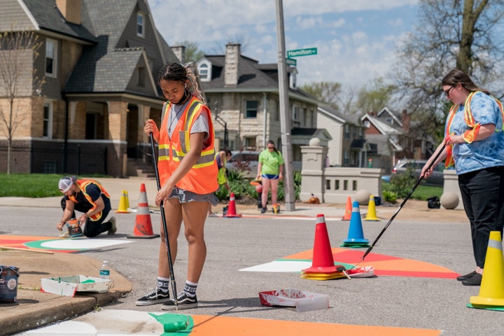 People work to paint a series of orange and red radial designs on a neighborhood street.