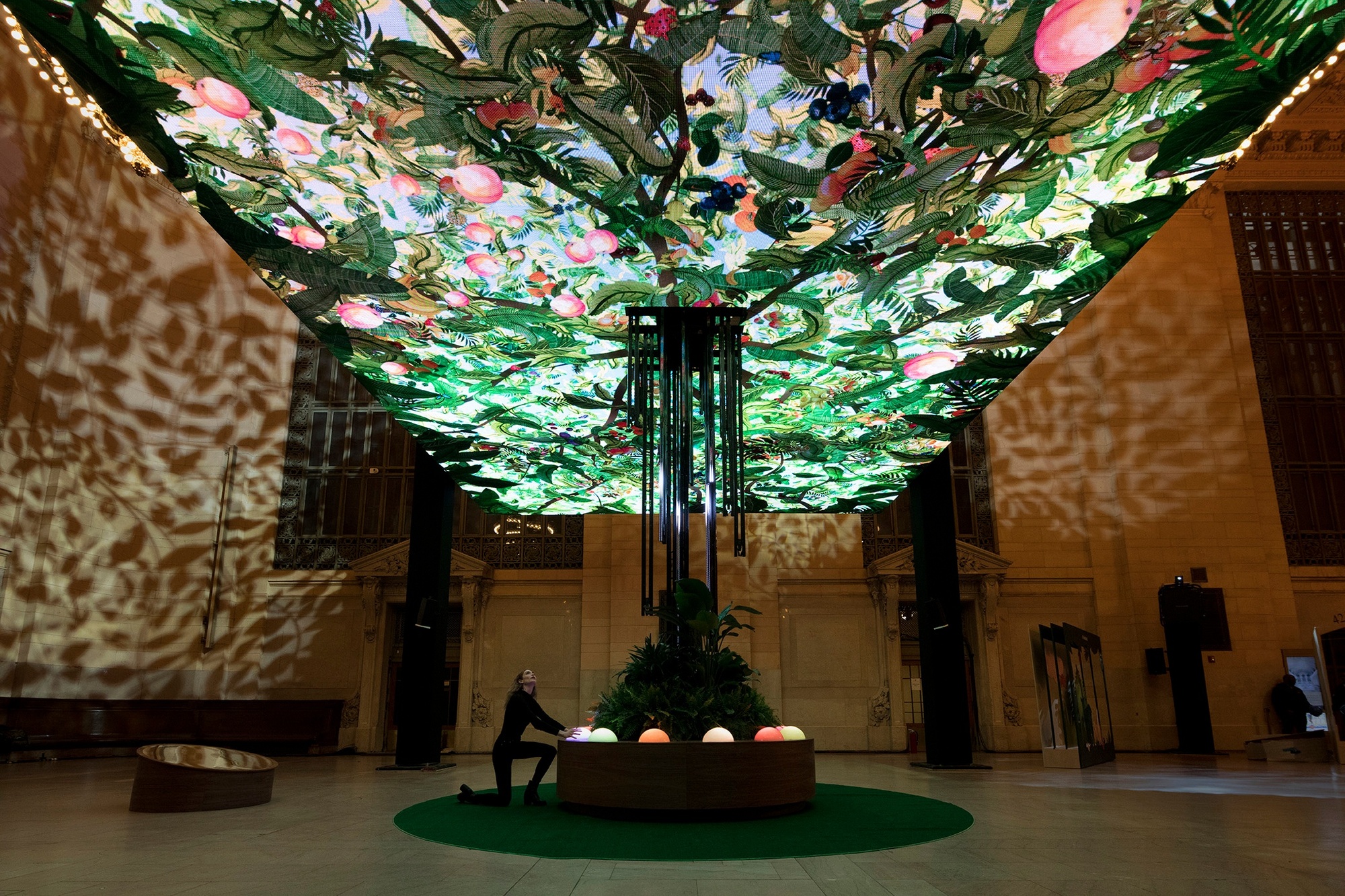 Young woman kneeling and placing hands on the orb of the Chobani Giving Tree installation