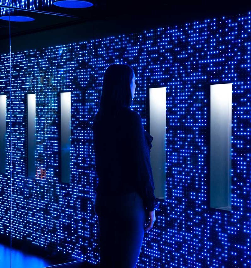 Young woman standing in front of wall of LED fixtures that shine with blue light