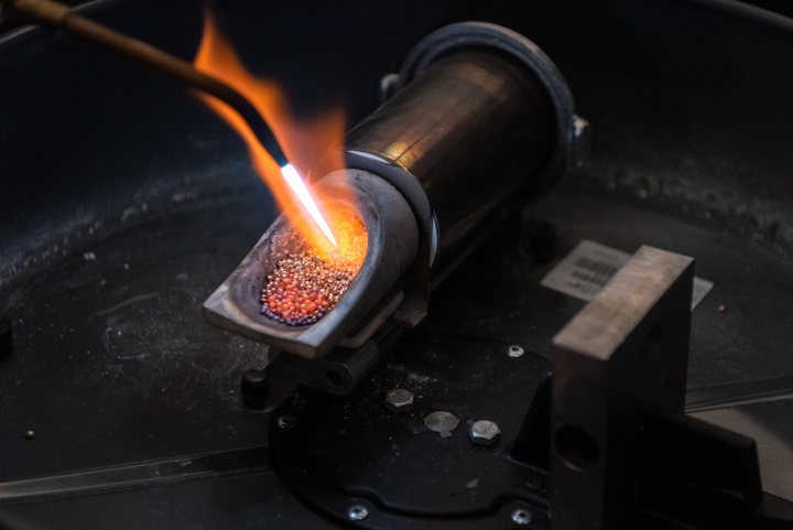 Close up of a torch melting bronze pellets in a crucible.