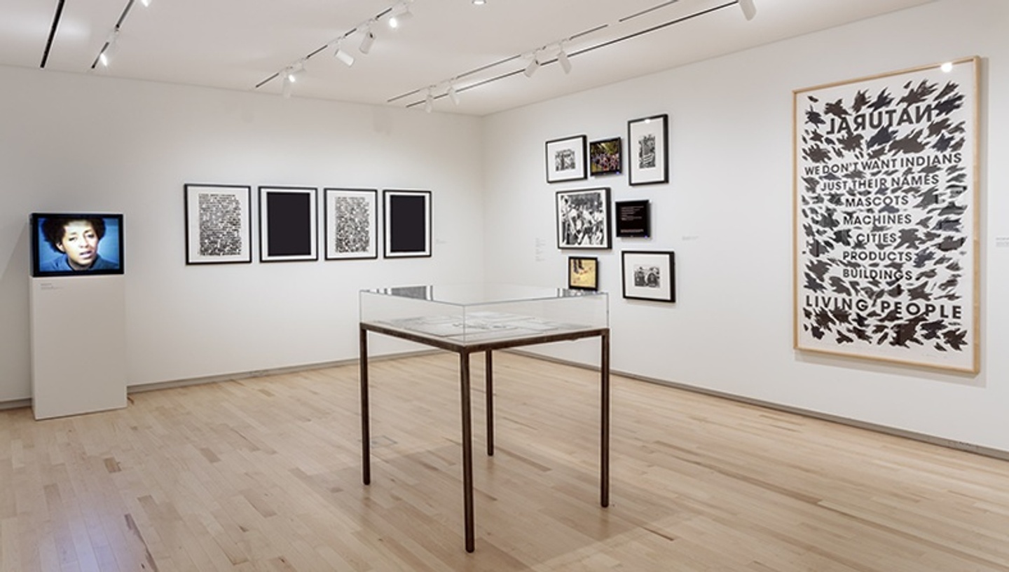 Installation view, Truths and Reckonings: The Art of Transformative Racial Justice inside the Kemper Art Museum, with artworks and video monitors on the walls and a vitrine in the middle of the space.