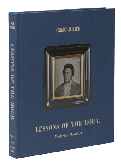 The front cover of Lessons of the Hour at an angle; the front cover is blue with a photo of a dark-skinned man and gold lettering.