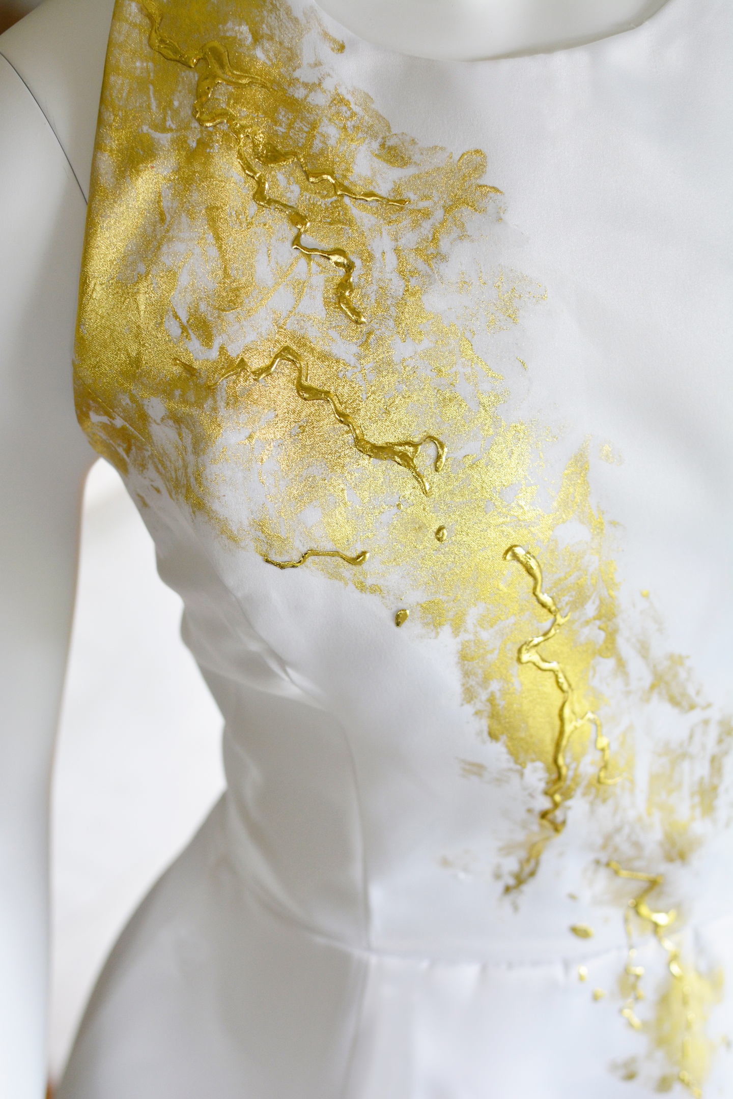 Detail of a white sleeveless dress with an abstract gold paint application running from the right shoulder down to the navel.