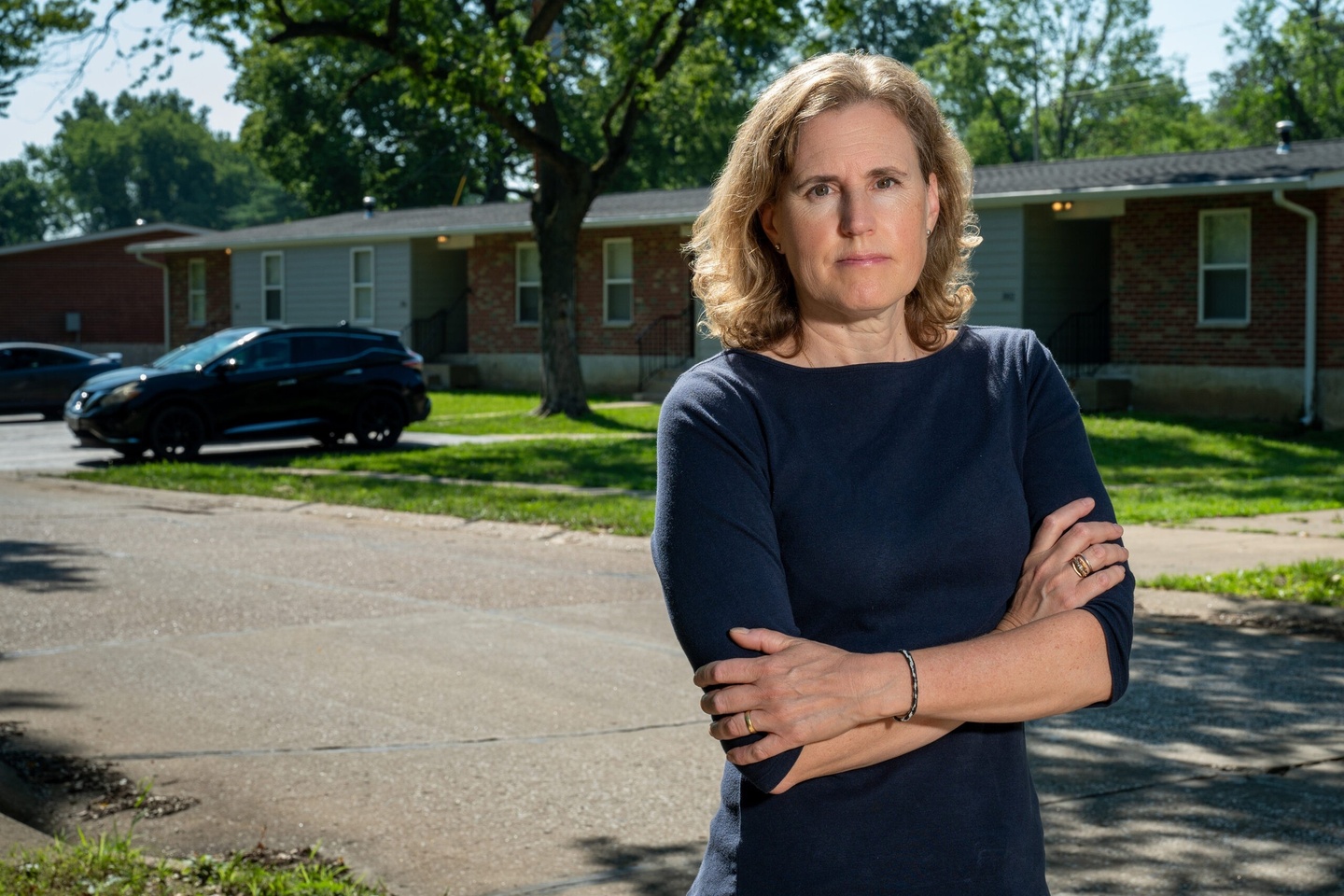 woman looking at camera with arms crossed with neighborhood street in background