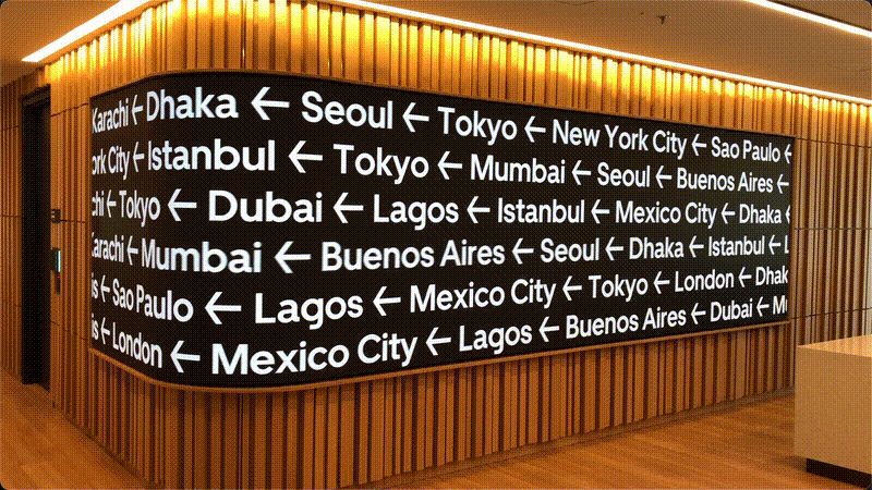 iew of high-resolution screen rounding around corner playing white text of city names on black background on wooden wall