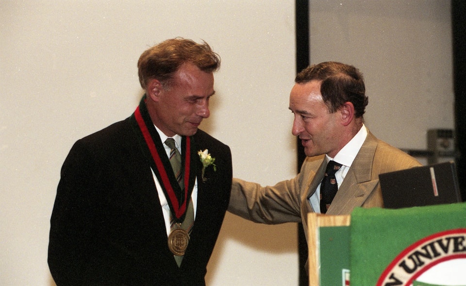 A man with a medallion is congratulated by another man.