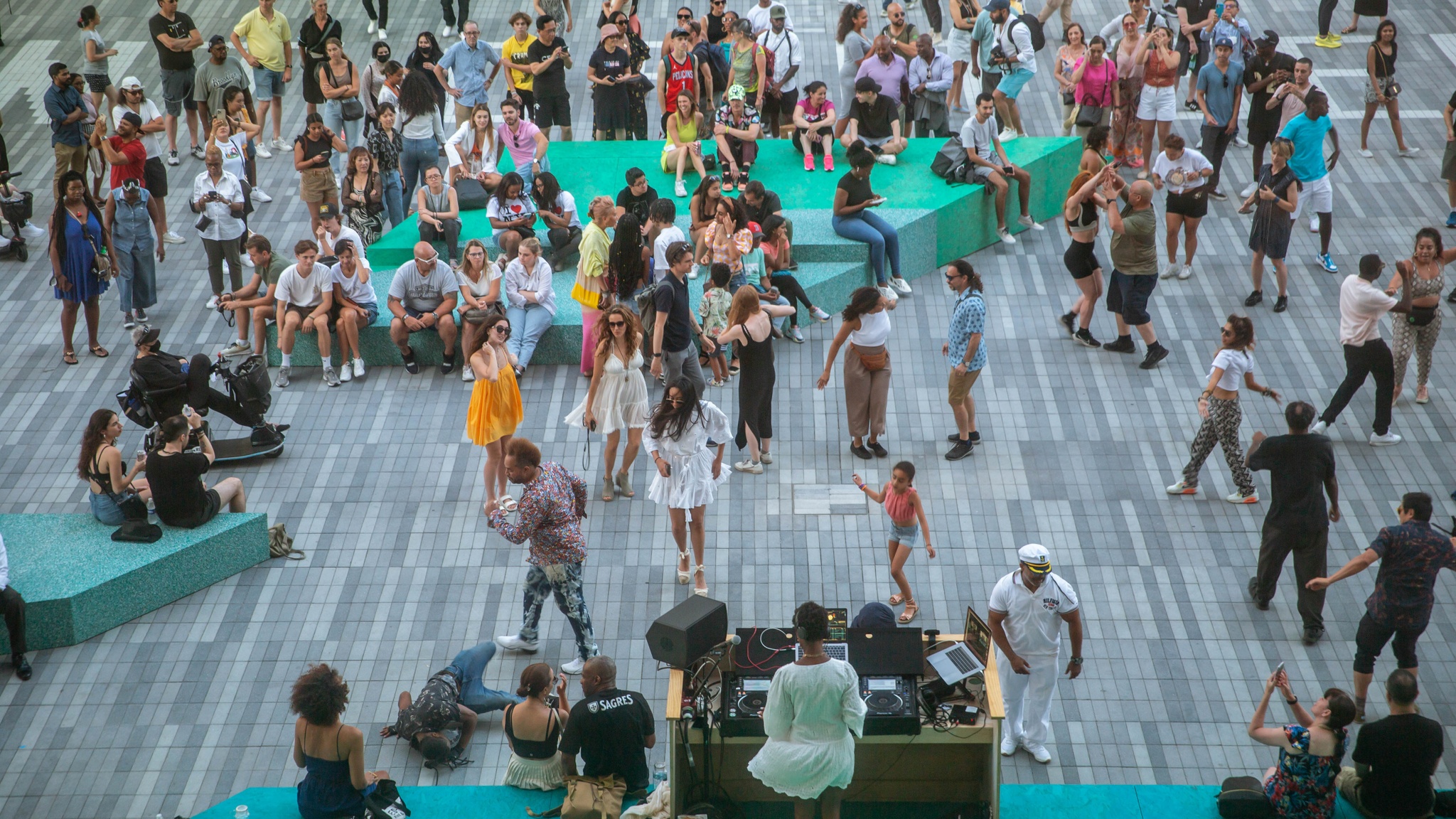 An aerial view of The Shed's outdoor Plaza where a crowd dances in the summer while a DJ in a short white dress being blown in the breeze spins.