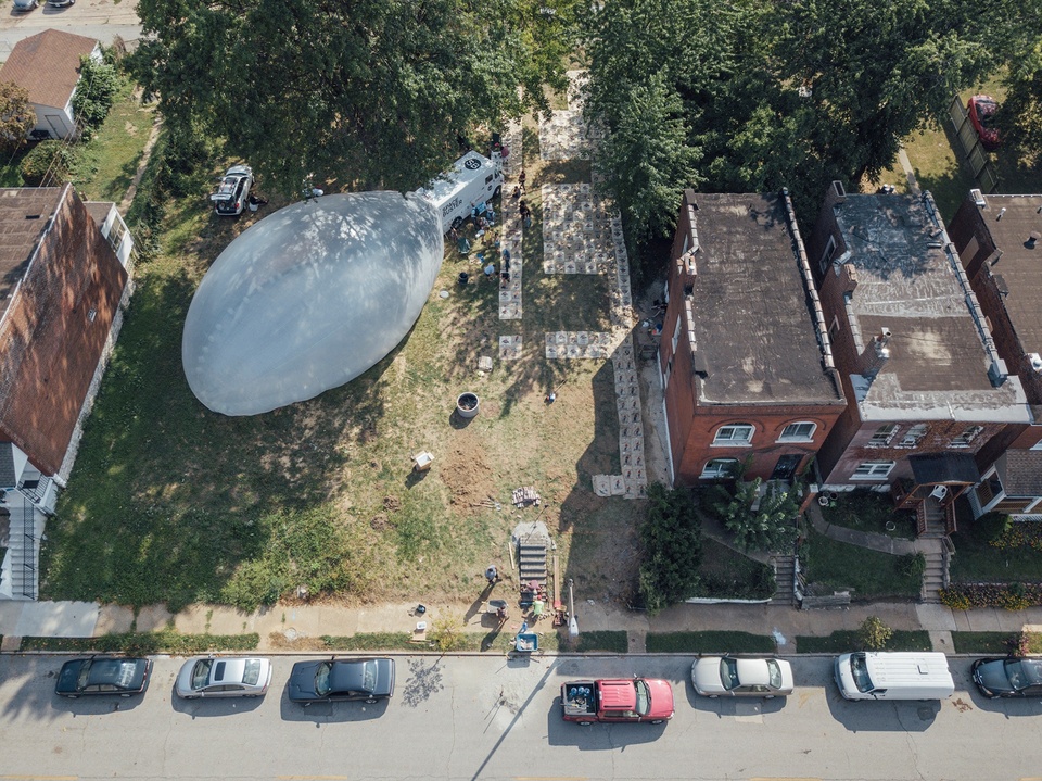 An overhead view of a lot between houses, with coffeebags laid out on the ground and a big plastic bubble. 