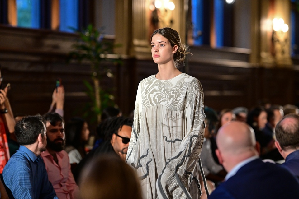 A model walking down the runway in a grey flowy dress with swirl patterns