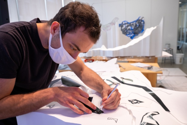 Person carefully affixes black vinyl decals to a white topographic model.