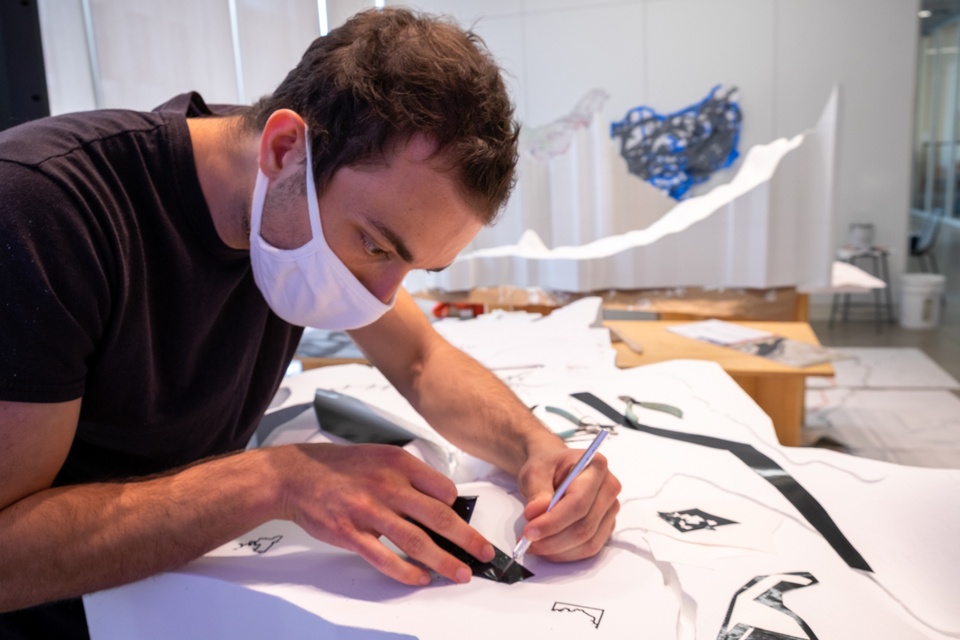 Person carefully affixes black vinyl decals to a white topographic model.