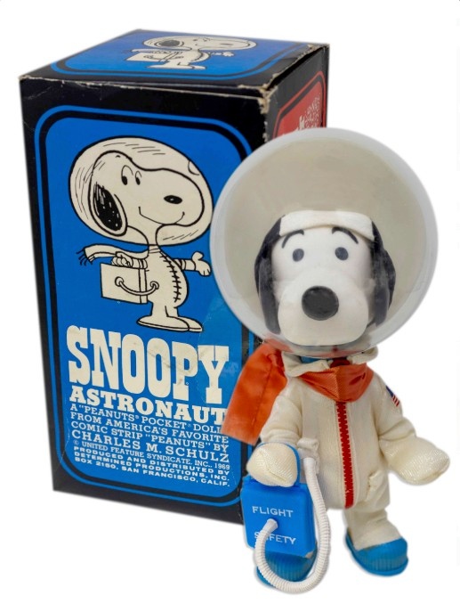 A photograph of a child's toy of Snoopy the dog dressed as an astronaut propped to the right of the box it came in.
