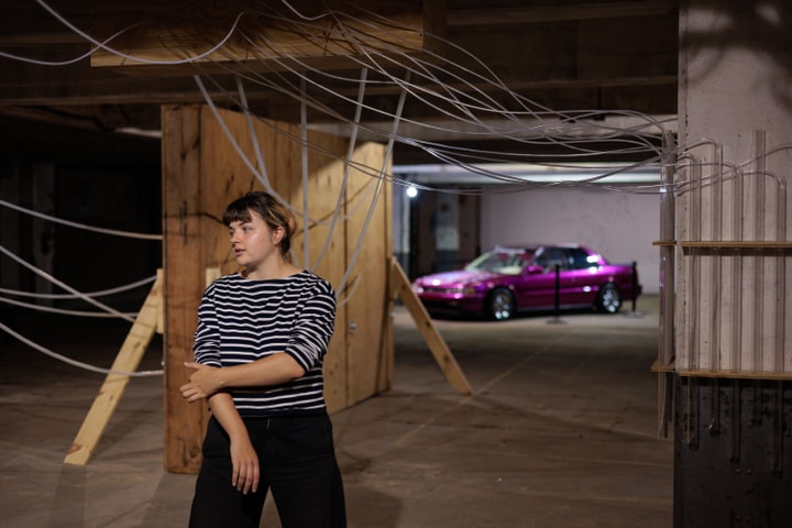 A woman wearing a striped shirt looks into the distance while standing in front of two art installations.
