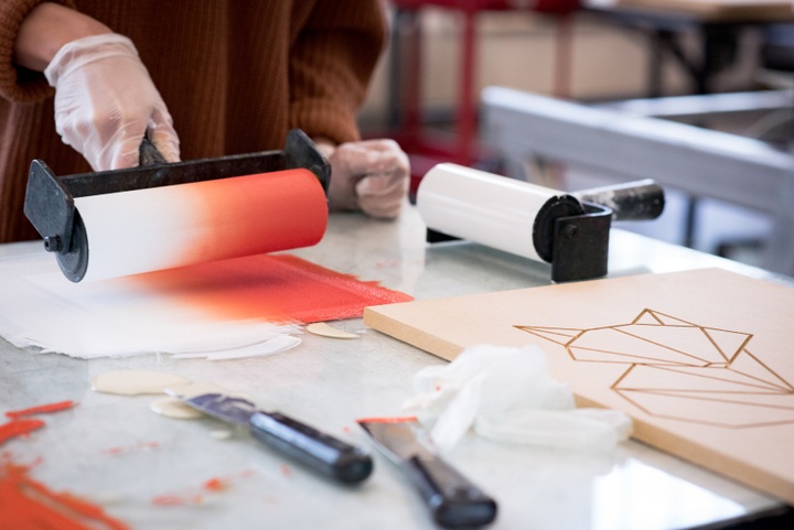 Close up of an orange and white rainbow roll being applied to a brayer. In the corner is a wood printing block with a relief cut of a fox.