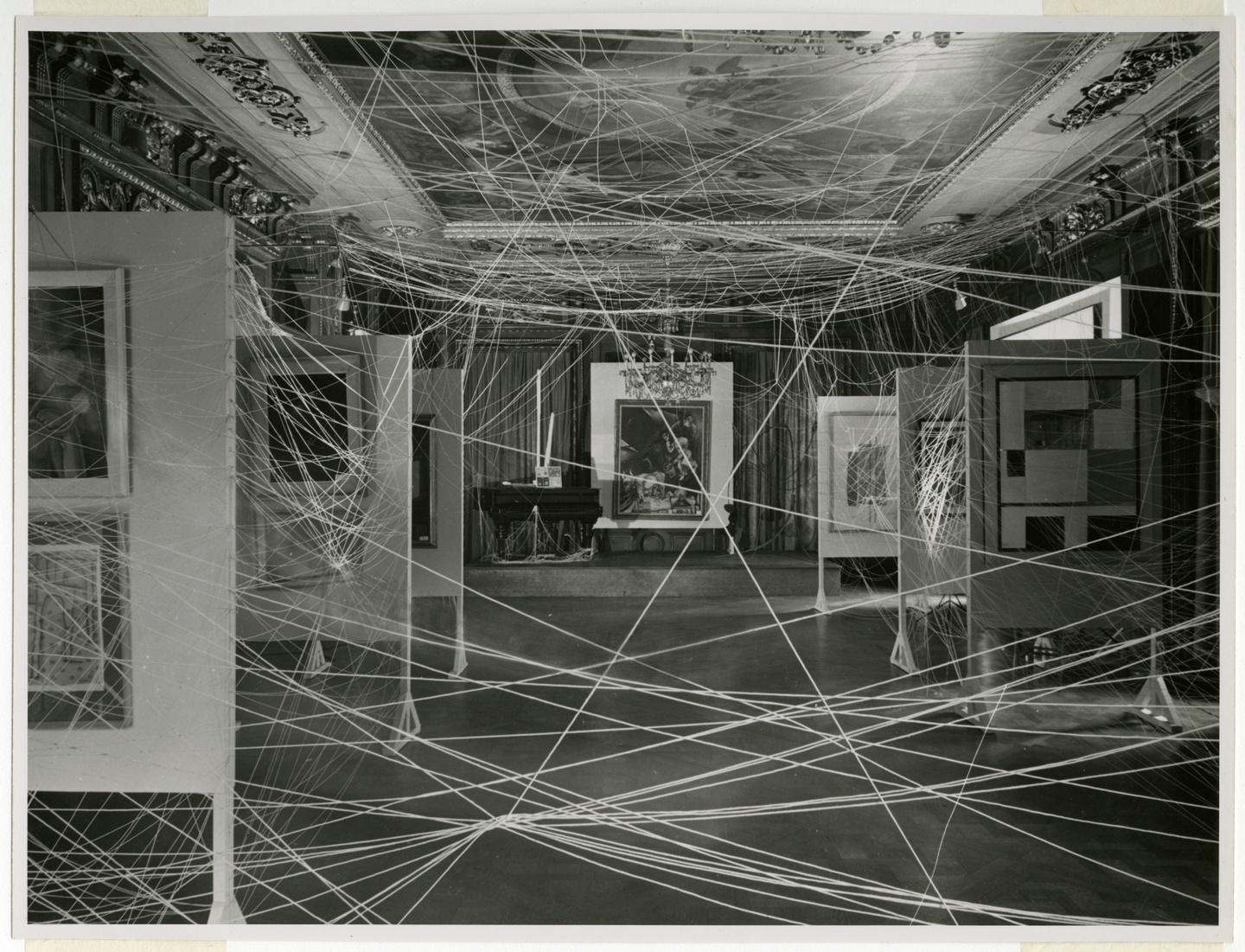 Black-and-white photo of a gallery space with string strung throughout