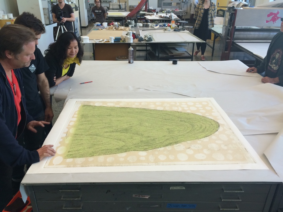 artist and others viewing an early proof of the mountain image on a table in the print shop