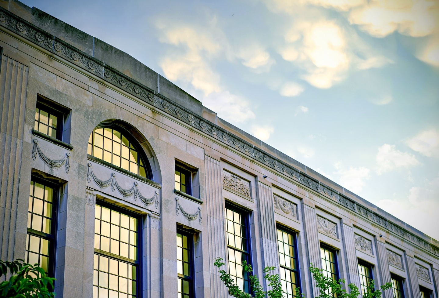 photo of a close up of a gray building with sunlight reflecting off the tall windows with a little bit of blue sky and clouds in the upper right corner