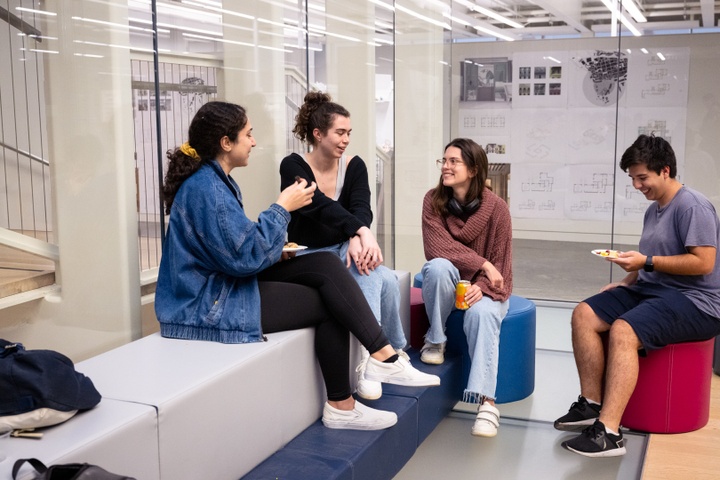 Four students sit on funky padded seating in a common space and chat.