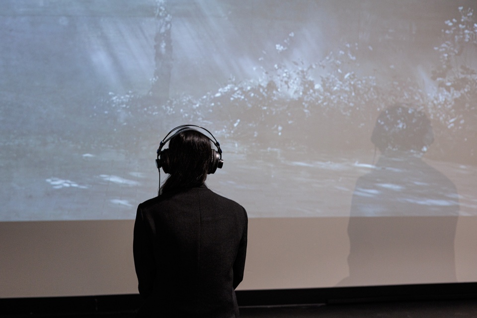 the artist with her back to us wearing headphones standing in front of a large screen