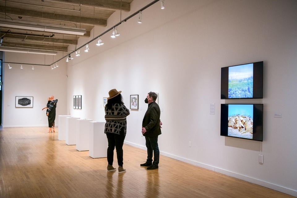 Two people stand and talk in a gallery space.