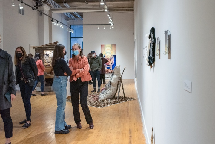 Crowd of people chat with each other in a small gallery space.