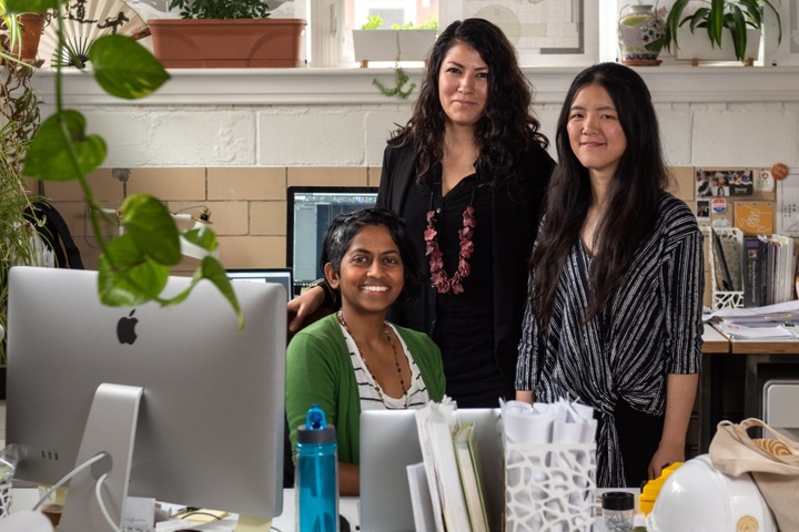 Three people posing for a photo at a desk in an office space filled with plants.