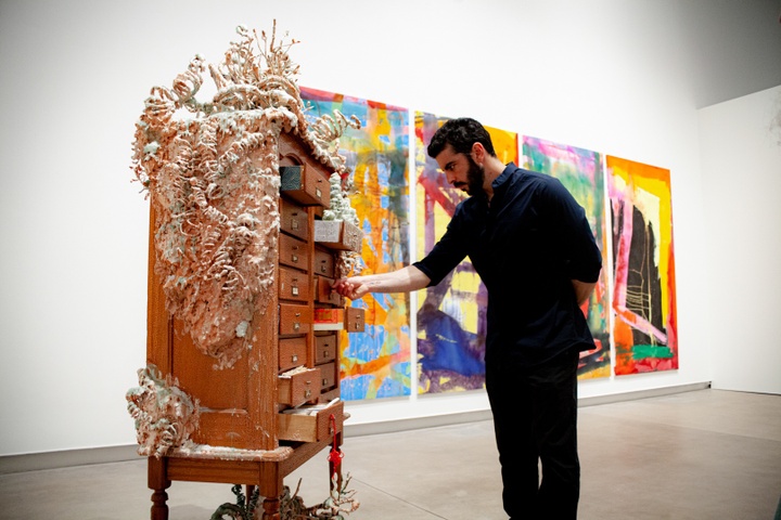 Gallery visitor opens a drawer in an upright wooden cabinet that has been covered in what resembles a pale, fleshy-colored fungal growth.
