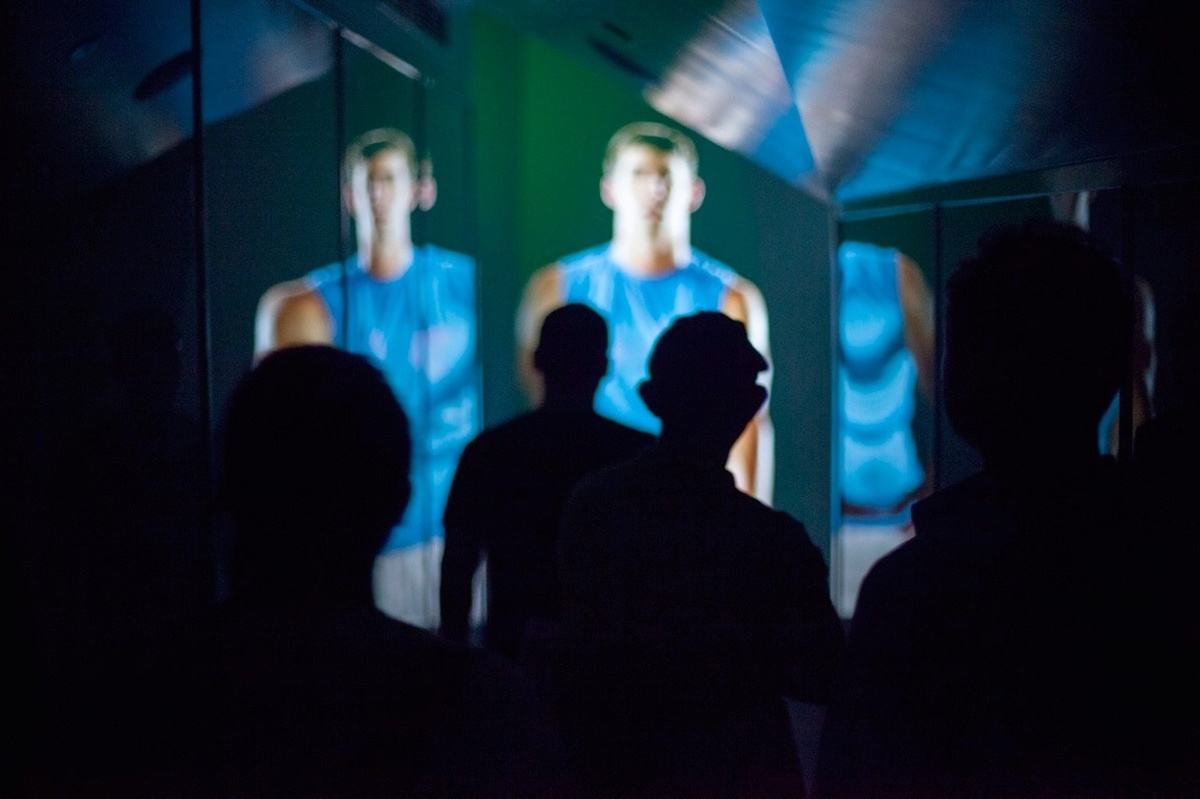 A group of silhouetted people approaching angular screens that showcase famous athletes
