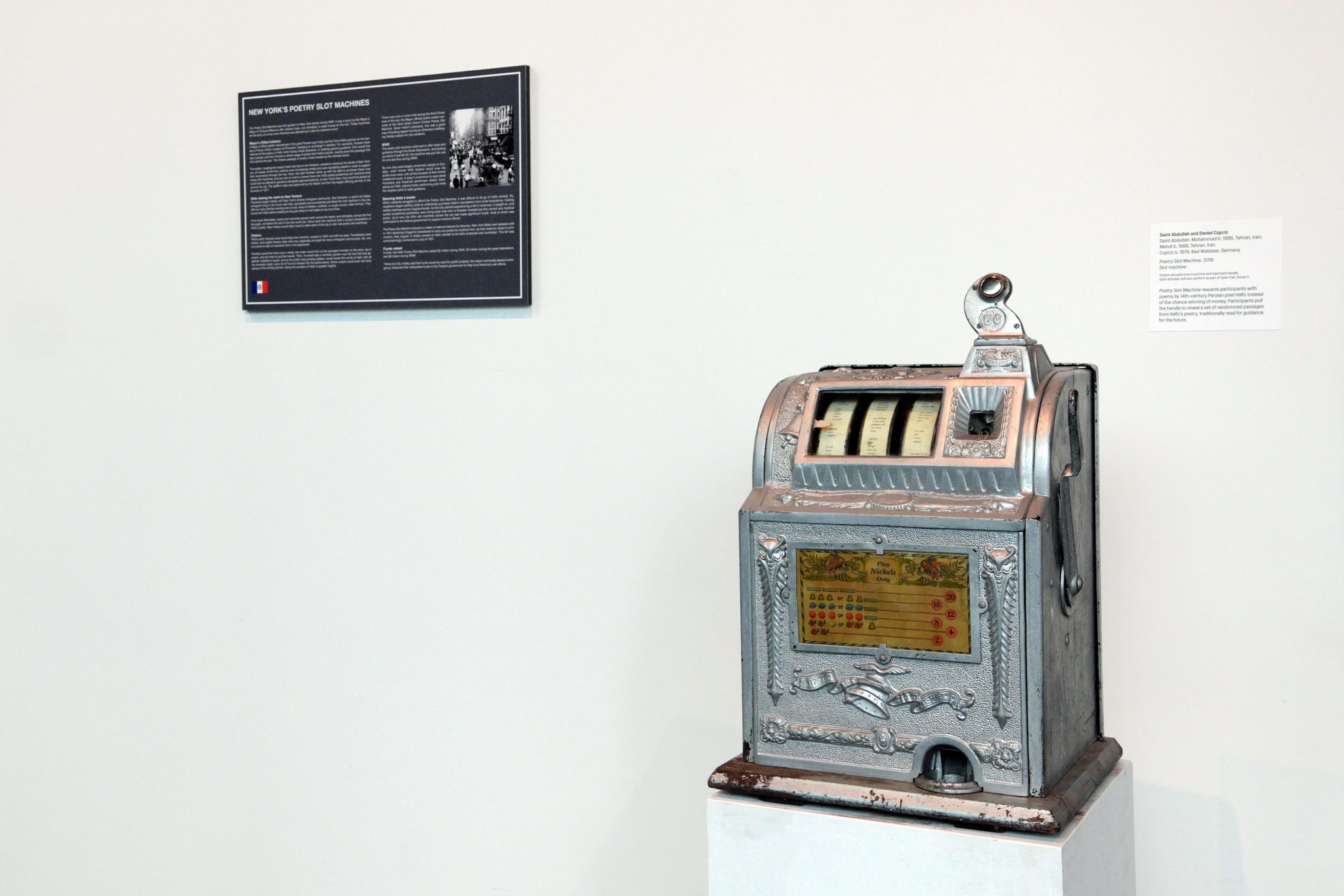 Silver vintage-looking machine in front of blank white wall.