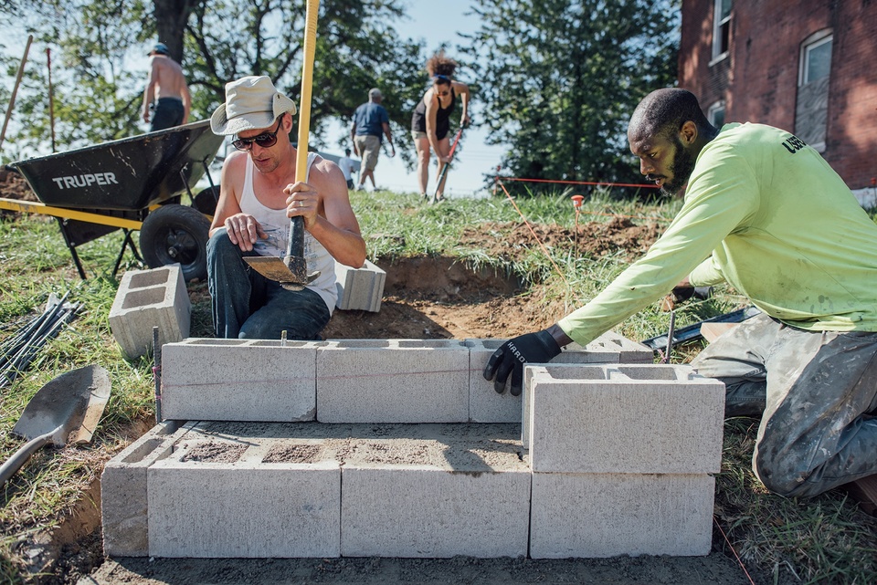 Two people assemble cement blocks into a wall structure. 