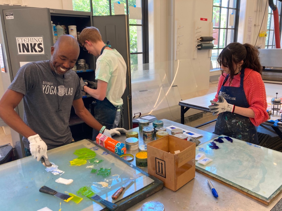 Artist, Barber, mixing different color inks on a glass slab while interns work behind him