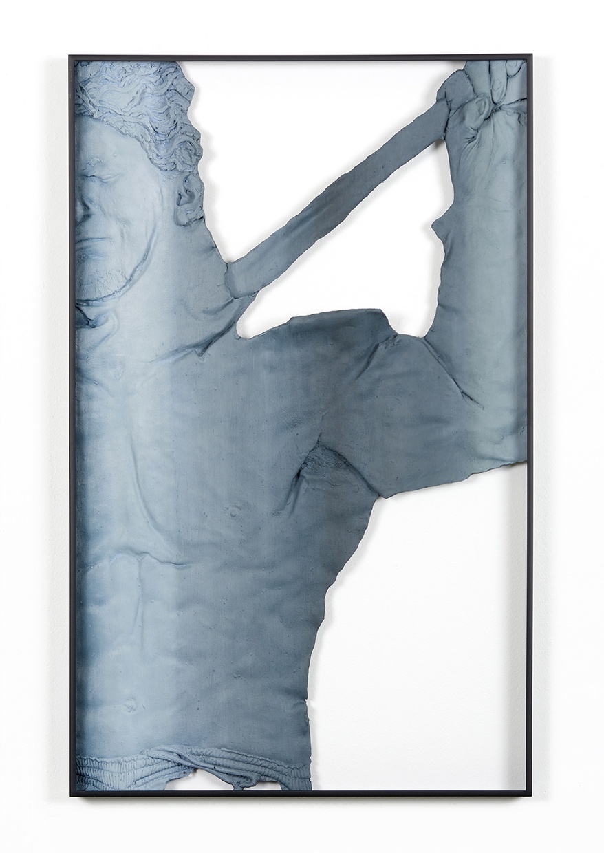 A sculpture of a shirtless male figure in blue/gray tones with a white background. A black frame surrounds the figure and it's hung on a white wall.