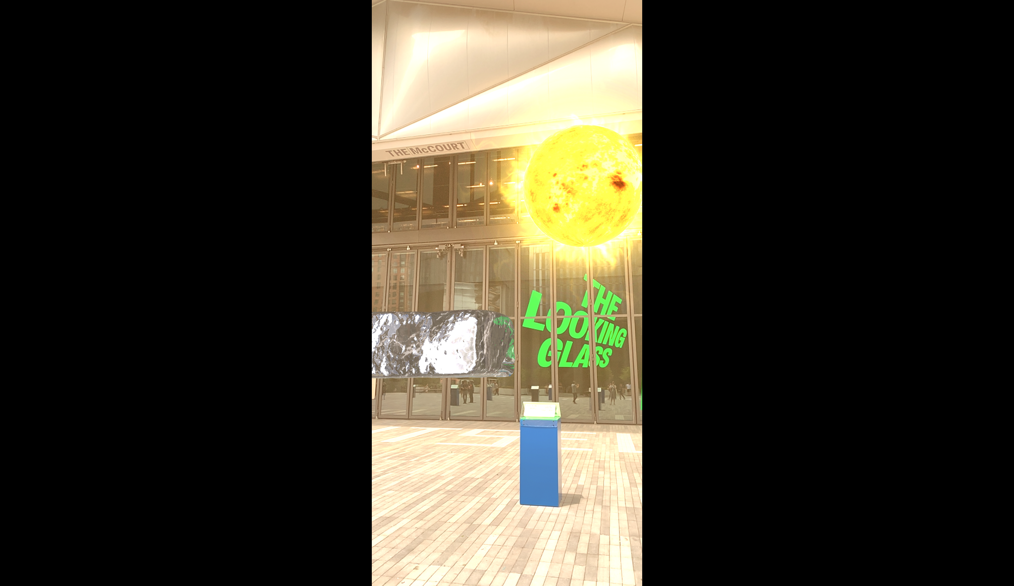 An augmented reality ice cube and blazing sun hang over an outdoor plaza