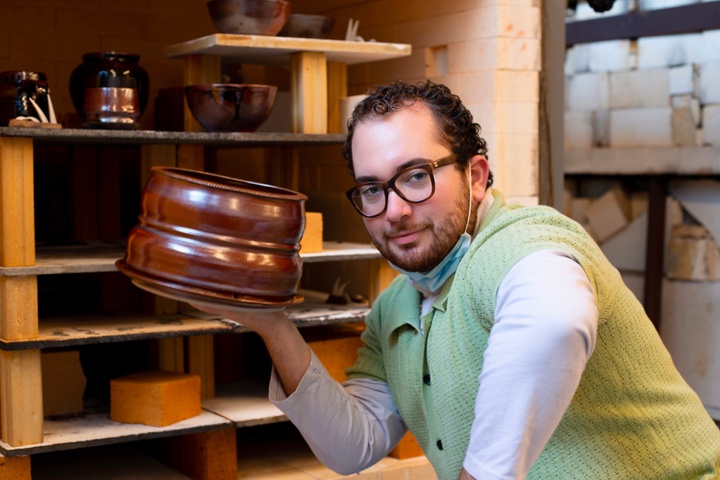 Photo of William Satloff in front of shelves of ceramics, holding a large bronze vessel.