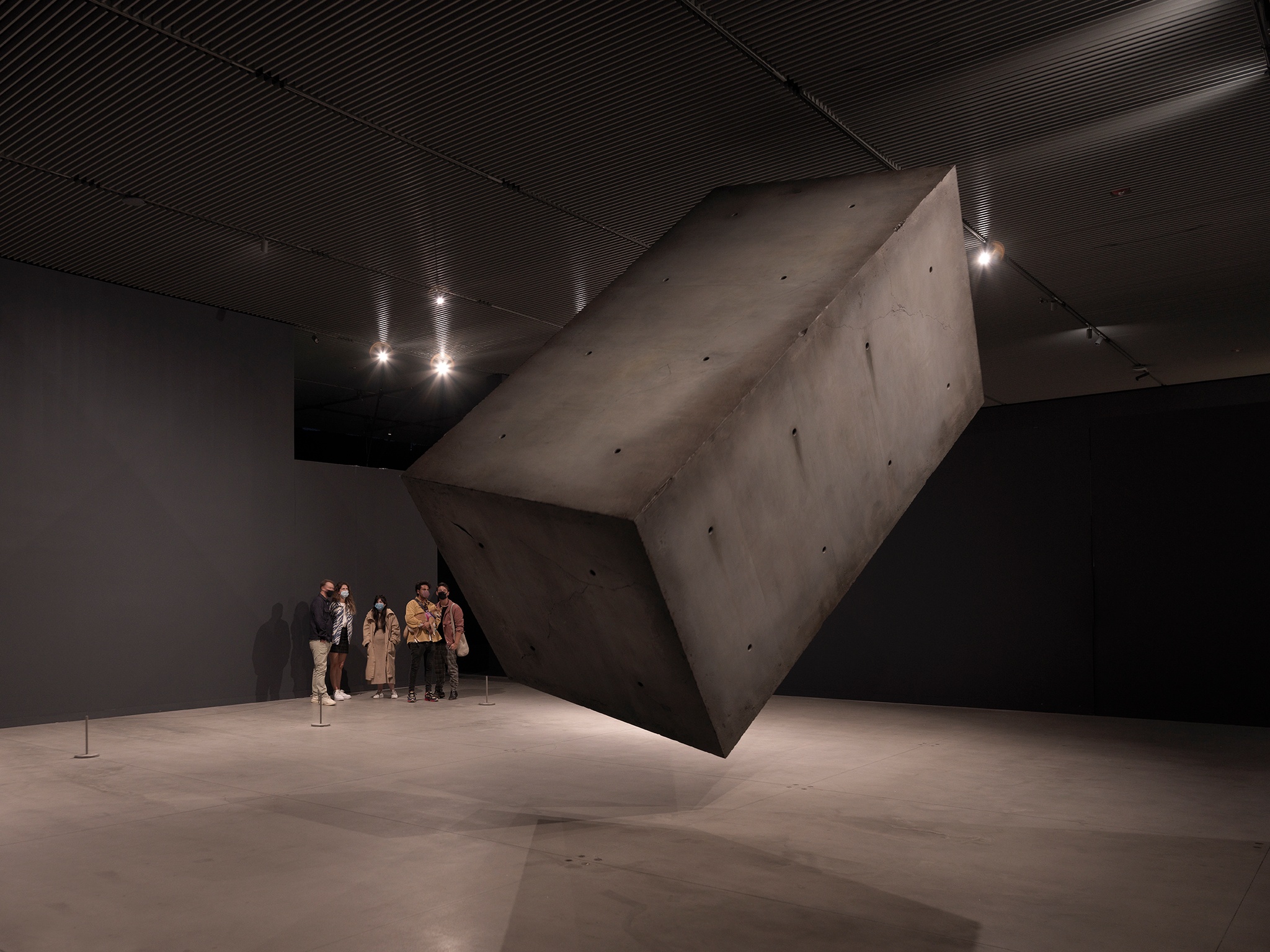 Gallery visitors standing against a wall with a concrete block floating midair in front of them