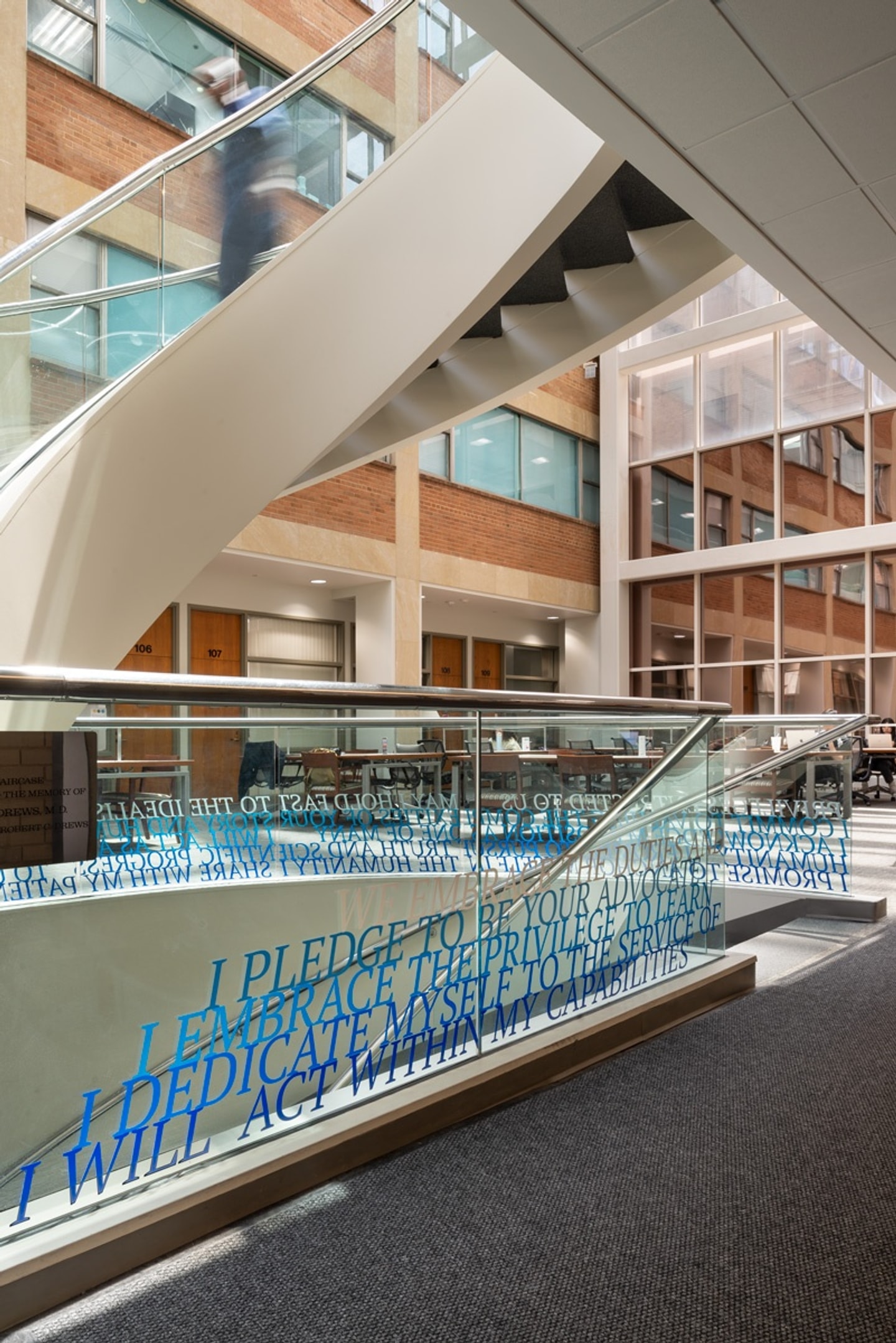 A staircase with glass sides and the hippocratic oath installed in blue vinyl