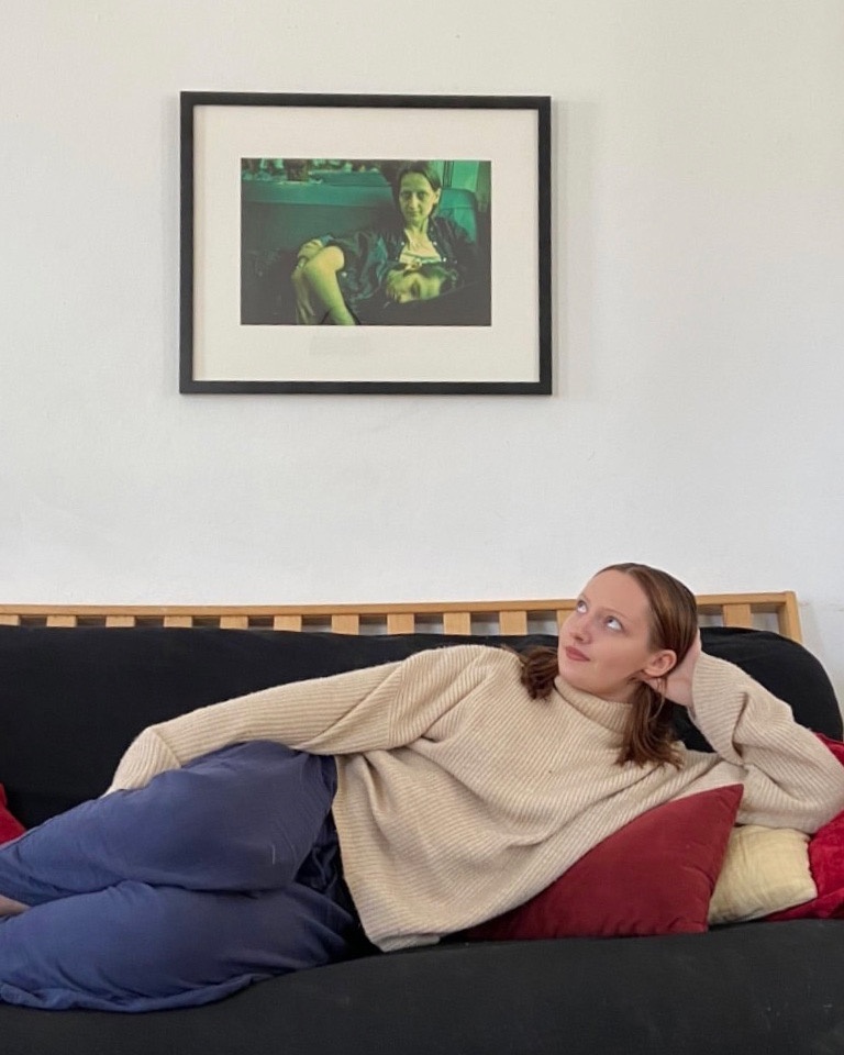 A student reclines on a sofa beneath an artwork on her wall.