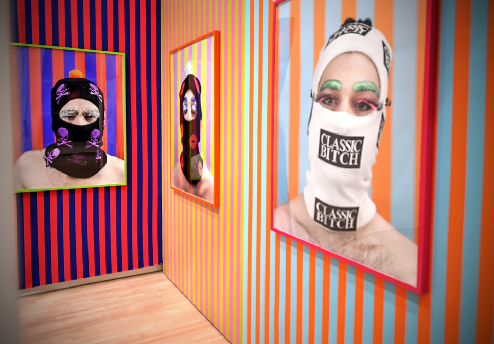 Three photographs hang in the corner of a gallery. The walls have striped wallpaper.