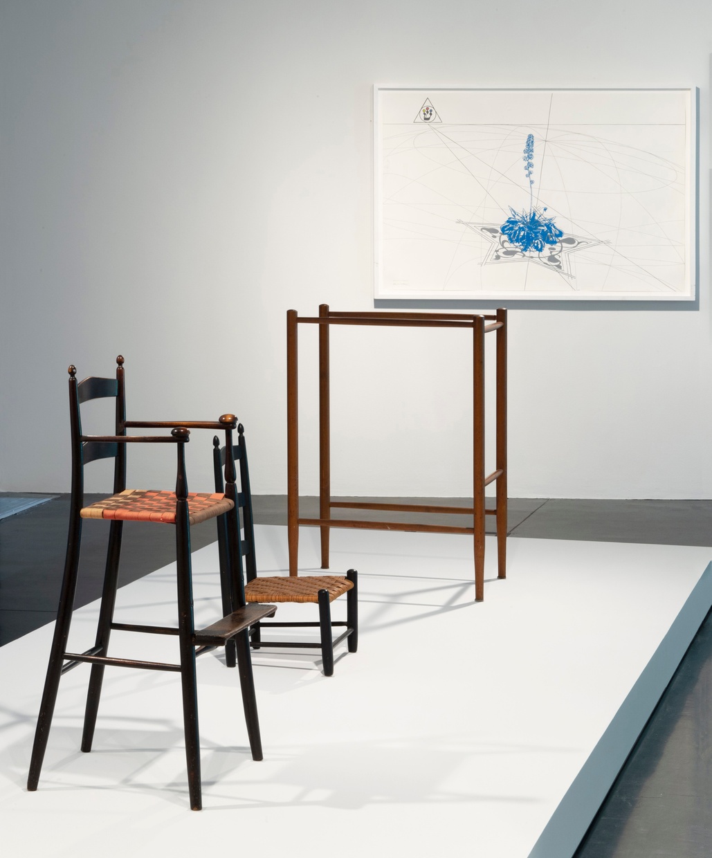 Wood furniture is arranged on a white surface and behind them is a white and blue grid artwork.