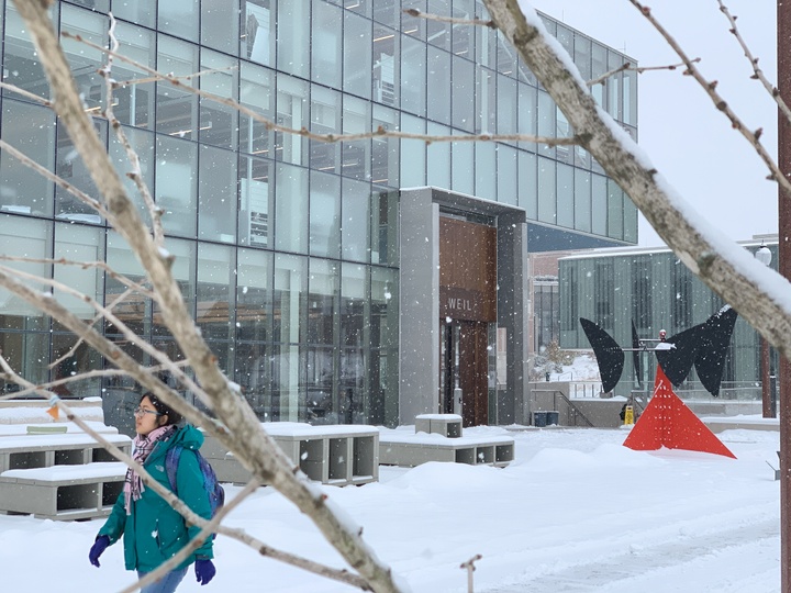 A student walks through snow drifts outside Weil Hall. The bright red Calder sculpture stands out against the snow.